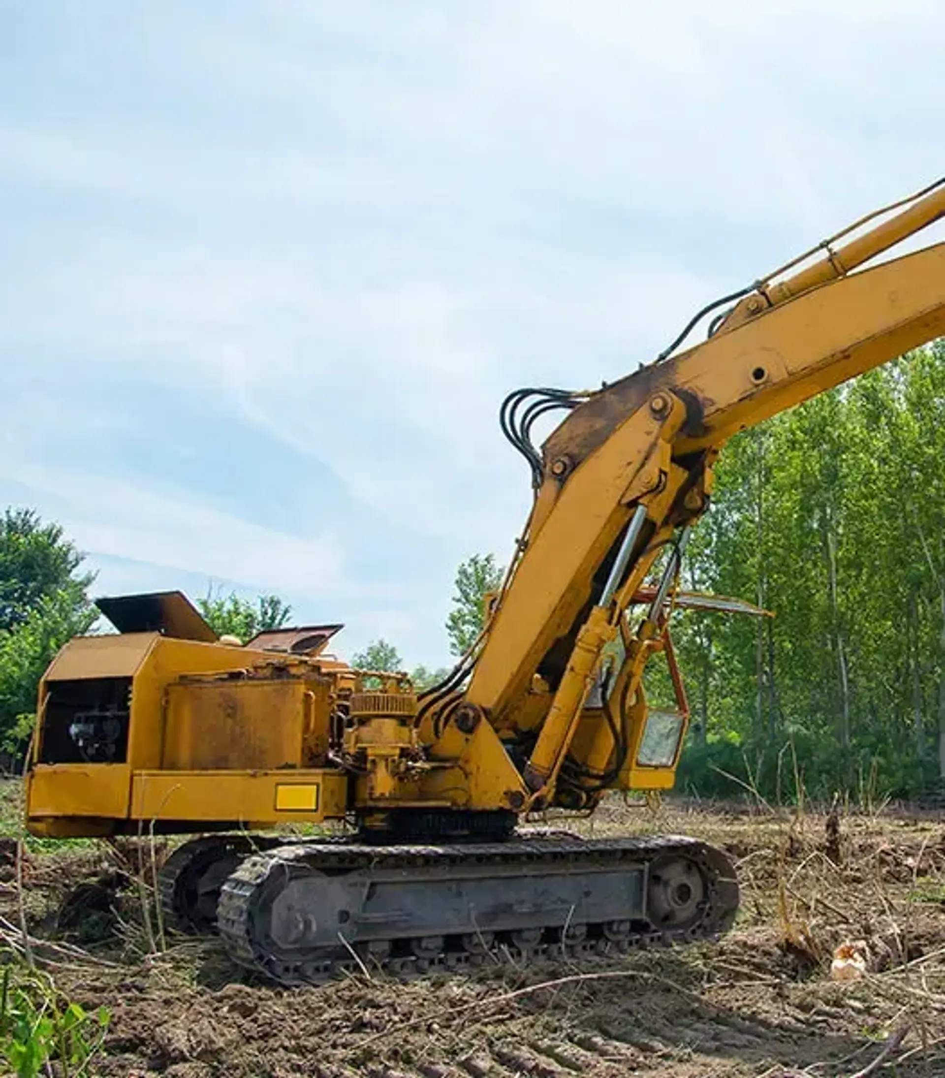 Yellow tracked excavator on a cleared dirt lot surrounded by trees