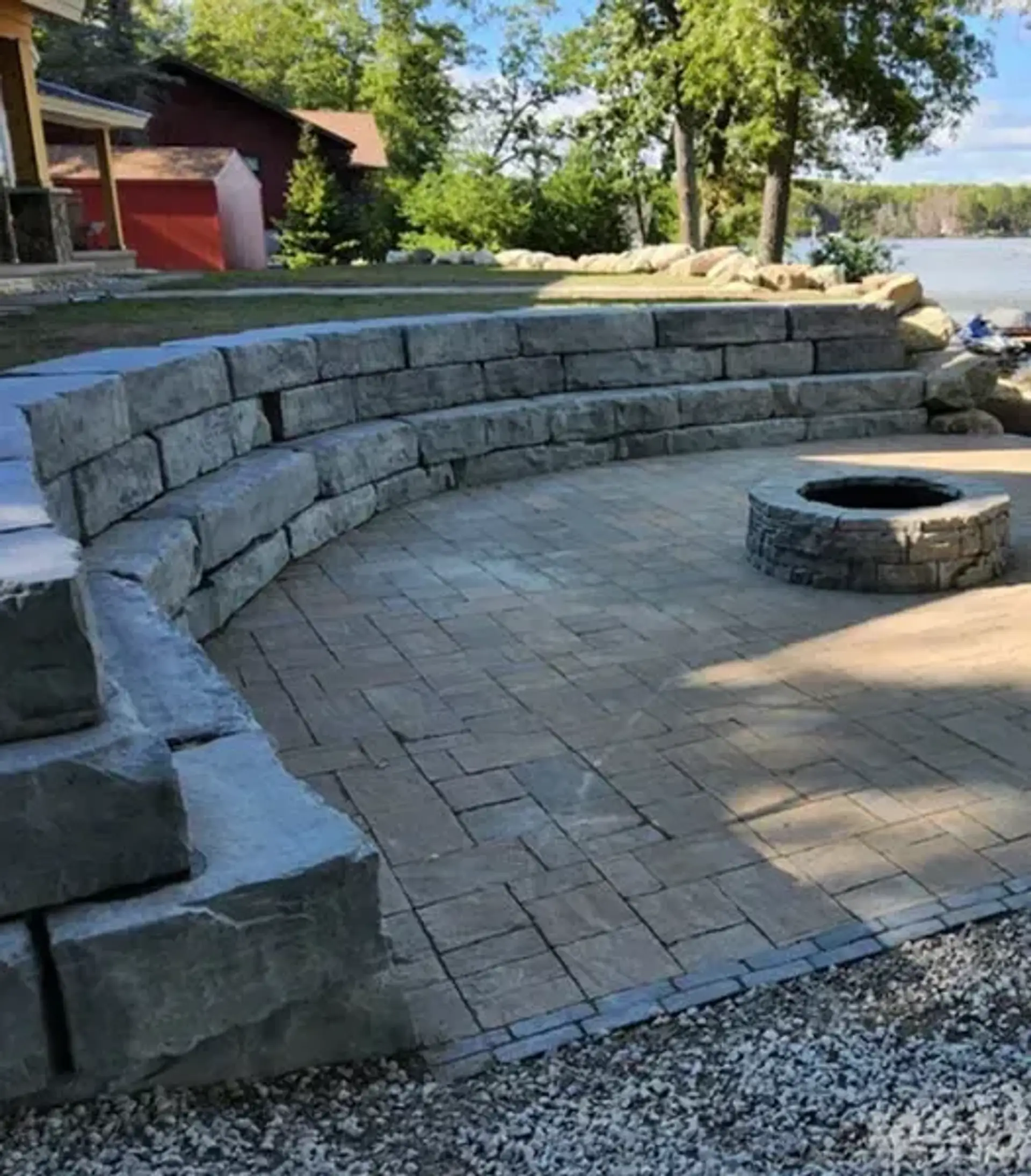 Curved stone seat wall around a paver fire pit patio with a lake in the background