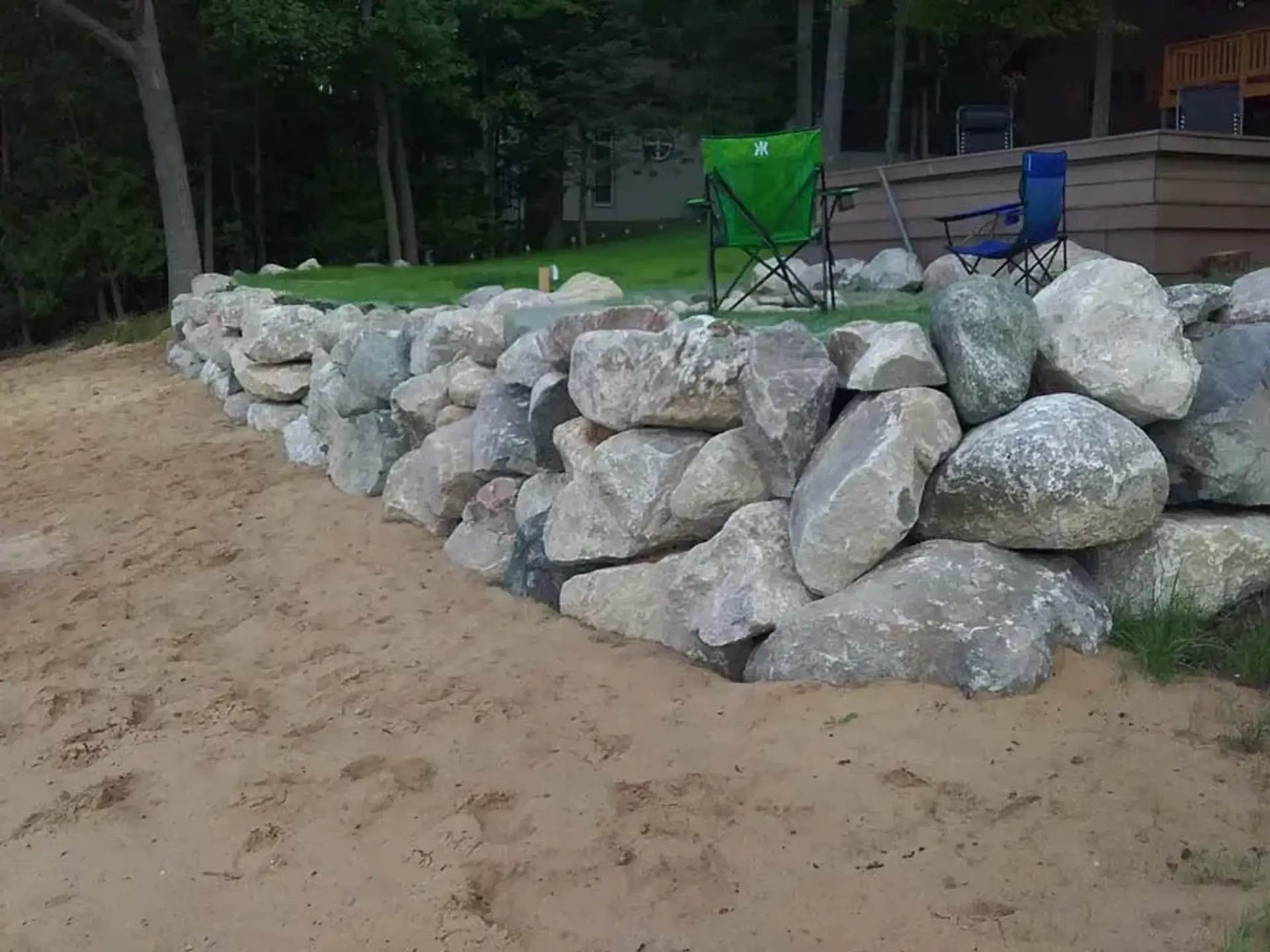 Large gray boulder retaining wall holding a lawn above a sandy beach
