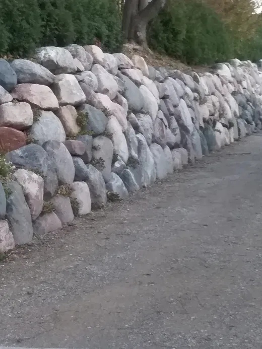 Tall stacked boulder wall running along a paved drive