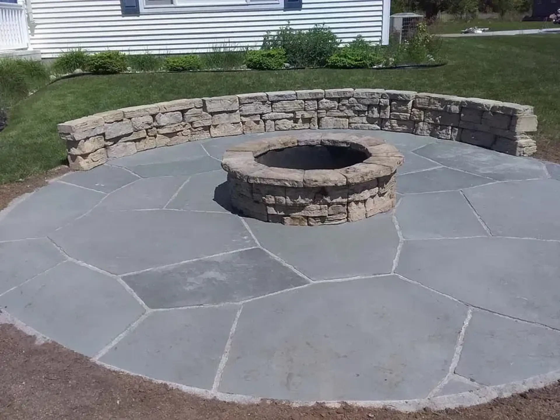 Round stone fire pit on a circular flagstone patio with a curved stacked stone seat wall