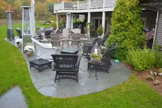 Curved bluestone flagstone patio with wicker seating and patio heaters beside the lawn