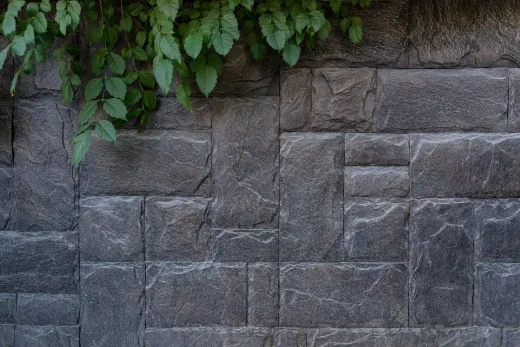 Close-up of a dark gray block retaining wall with ivy hanging over the top