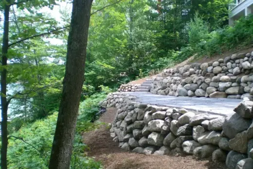 Terraced fieldstone retaining walls with stone steps and a paver landing on a wooded slope