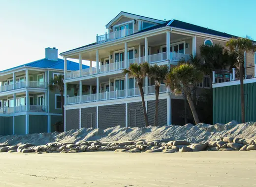 Large beach houses behind a sand dune and rock barrier