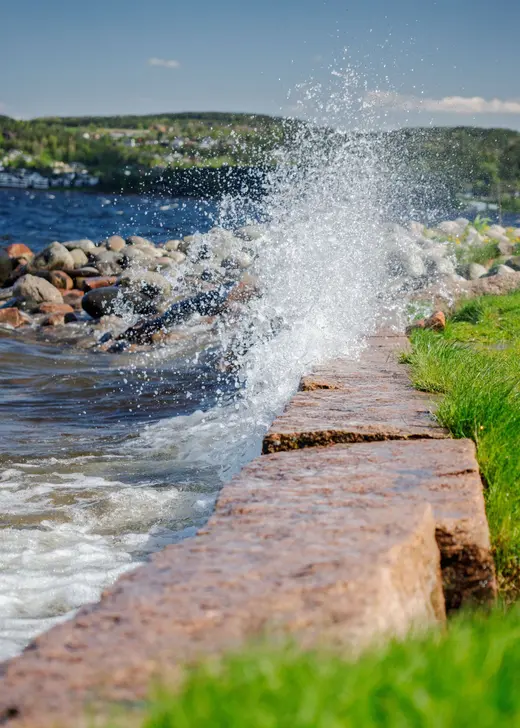 Wave splashing against a cut stone seawall with lawn behind