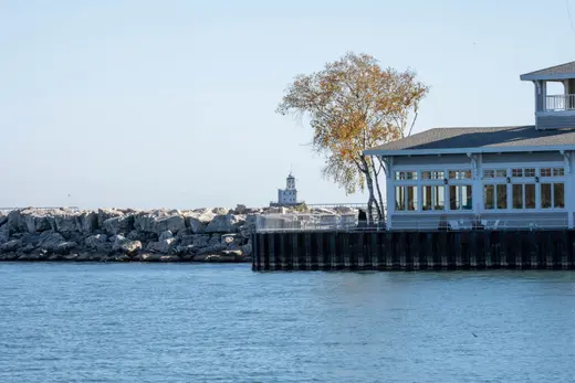 Harbor building on a steel seawall with a rock breakwater and lighthouse across the water