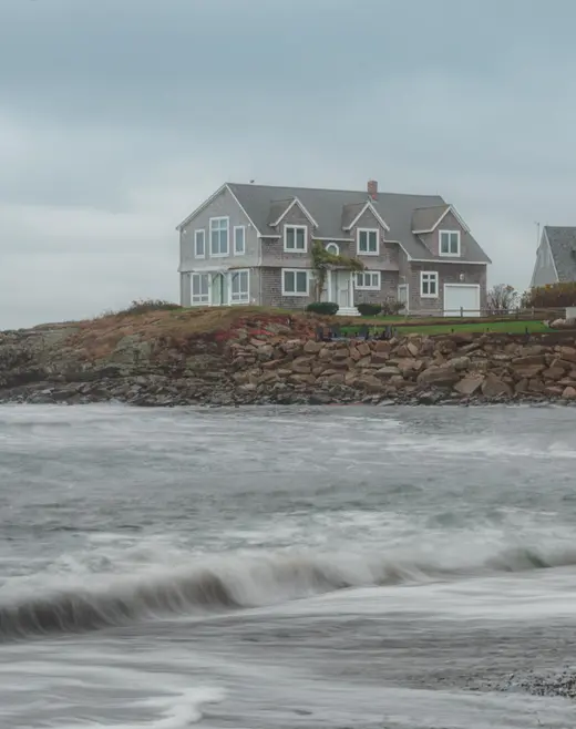Gray shingled house on a rocky point above breaking waves