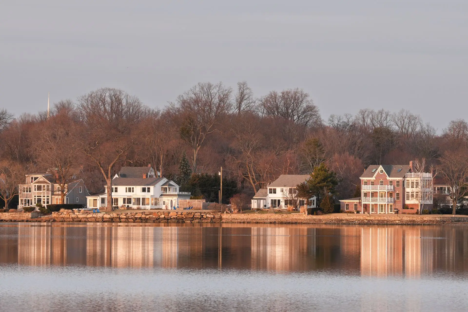 Waterfront houses behind a stone seawall reflected in calm water