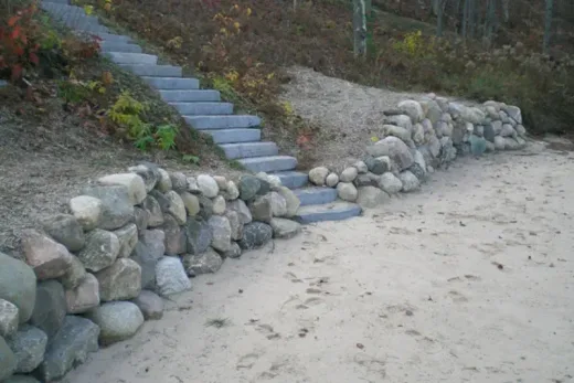 Long stone slab staircase up a wooded slope beside a fieldstone retaining wall