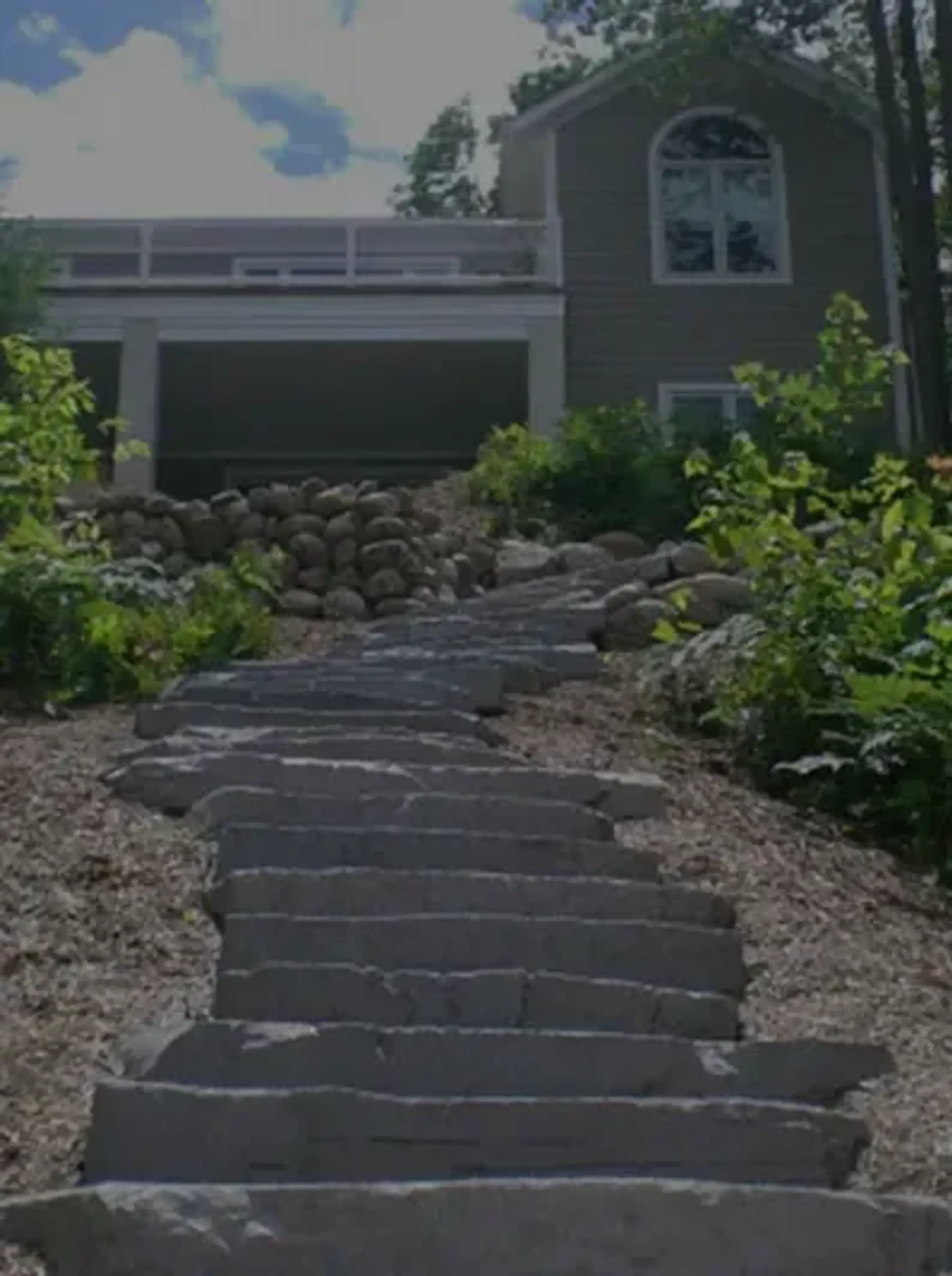 Natural stone slab steps climbing through gravel and plantings toward a gray two-story home
